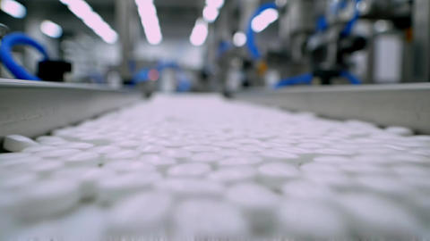 White pharmaceutical tablets moving conveyor belt close-up inside automated manufacturing facility