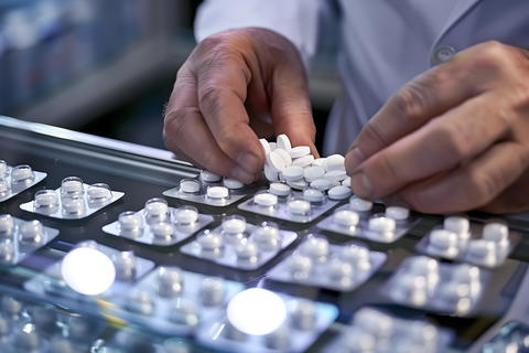 Pharmacist hands sorting white pills on blister packs at a modern pharmacy counter