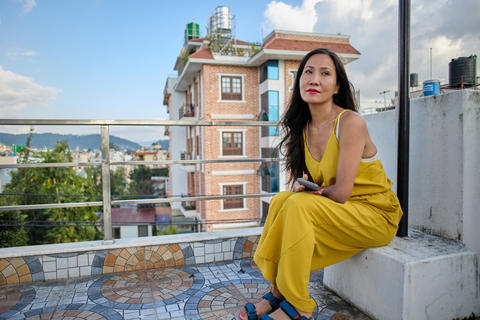 Female model in mustard dress sitting on rooftop ledge legs crossed gazing into