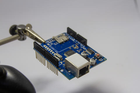 Microcontroller circuit board held by helping hands tool for electronics repair
