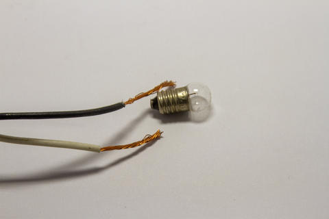Close up of a small incandescent light bulb with stripped copper wires on white background