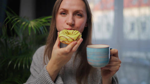Sweet addiction concept. A woman eats a donut and drinks coffee with pleasure