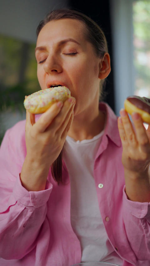 Woman with eating disorder eating two donuts with pleasure and at the same time