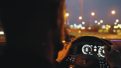 Backseat view on man driving car through the streets of the evening city