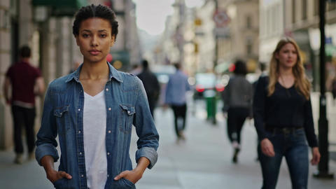 Young multiracial woman in denim shirt standing on busy city street, medium shot, eye level