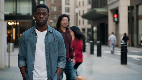 Young Black man in blue denim shirt standing on busy city street with people walking in background