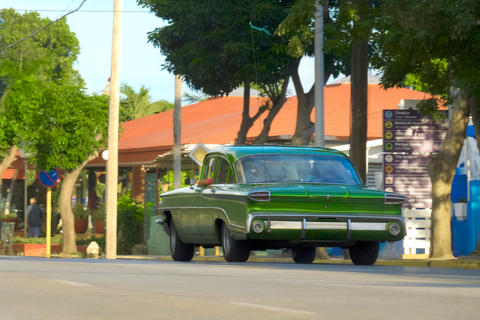 Classic green car driving along a quiet street. Retro vehicle, sunny day