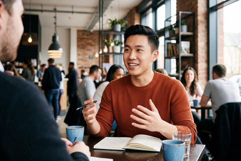 Smiling asian man talking during a casual business meeting in a modern cafe