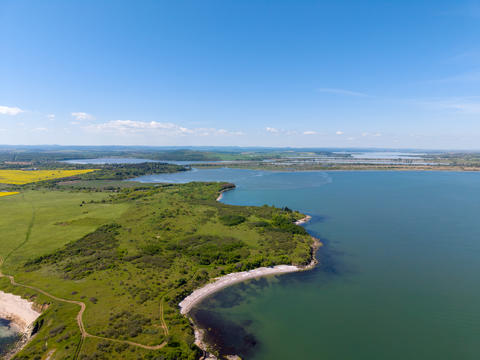View of coast and fields near water in sunny weather with blue sky