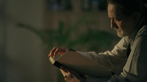 Elderly man reading a book in warm dim light at home
