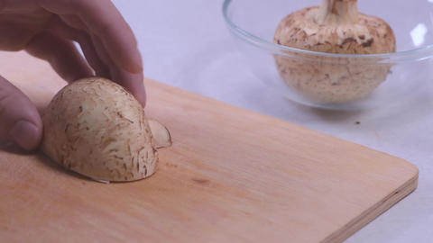 Fresh white mushrooms being sliced on a wooden cutting board with a glass bowl