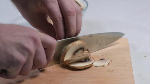 Chef's hands skillfully slice fresh mushrooms on a wooden cutting board, with a