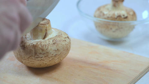 Fresh white mushrooms being sliced on a wooden cutting board with a bowl of