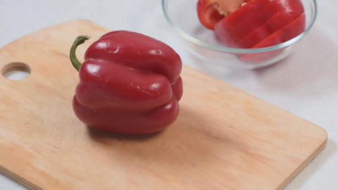 Red bell pepper placed on wooden cutting board while a hand slices it in half