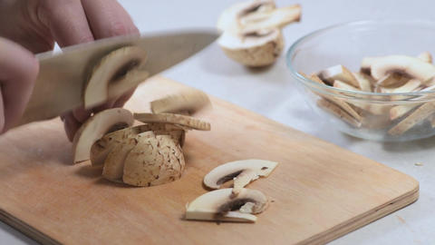 Sliced mushrooms on wooden cutting board with hand holding knife, preparing