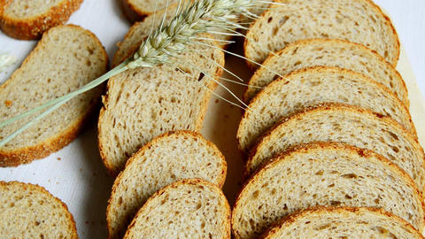 Slices of whole grain bread arranged on a white surface with a stalk of wheat