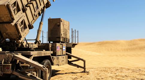A tan military missile defense system with US and Israeli flags stands ready in a vast desert landsc