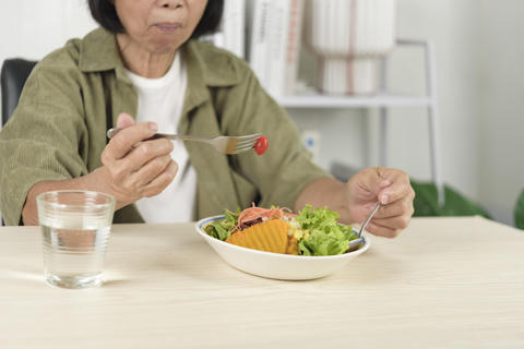 Senior Asian woman eating fresh vegetable salad with pumpkin and drinking water at home. Elderly hea