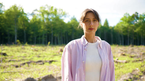 Caucasian female environmental volunteer standing on deforested land and looking at camera. Woman