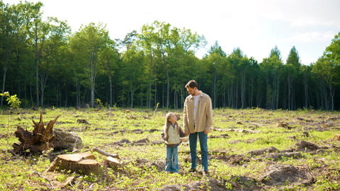 Caucasian father holding daughter hand on deforested land and looking at camera. Family witnessing