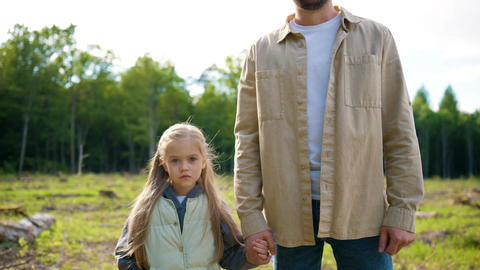 Caucasian father and little daughter standing on cleared forest land and looking at camera. Family
