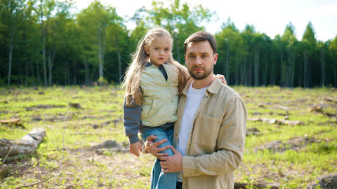 Caucasian father holding little daughter on deforested land and looking at camera. Family witnessing