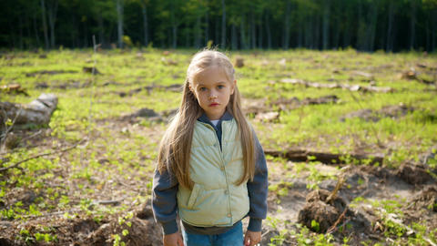 Close up of little Caucasian girl standing on deforested land and looking at camera. Child