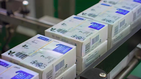 Finished medicine boxes stacking automatically, close-up view of packaged cartons moving a