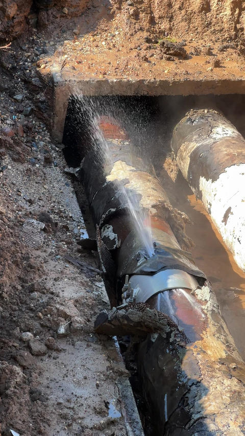 Broken heating pipe sprays water inside trench during utility accident, showing damaged insulation