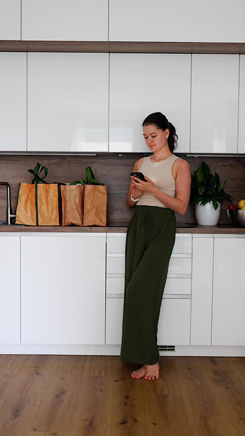 Woman checking grocery delivery with smartphone while unpacking reusable