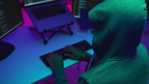 Hacker Typing Code in a Cyber Environment Surrounded by Computer Screens