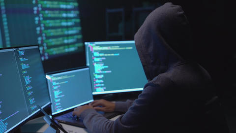 Hacker Typing Code on Multiple Screens in a Cybersecurity Environment