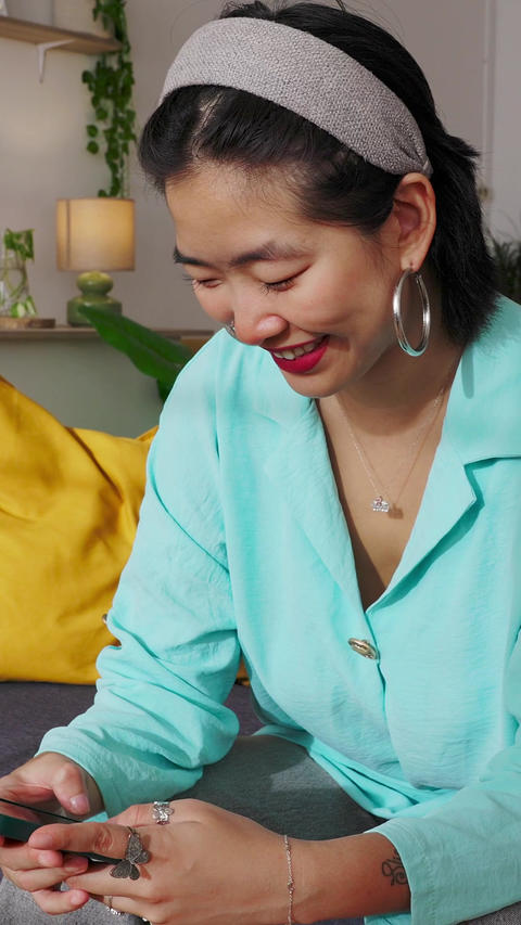 Smiling young adult asian woman checking her smartphone at home