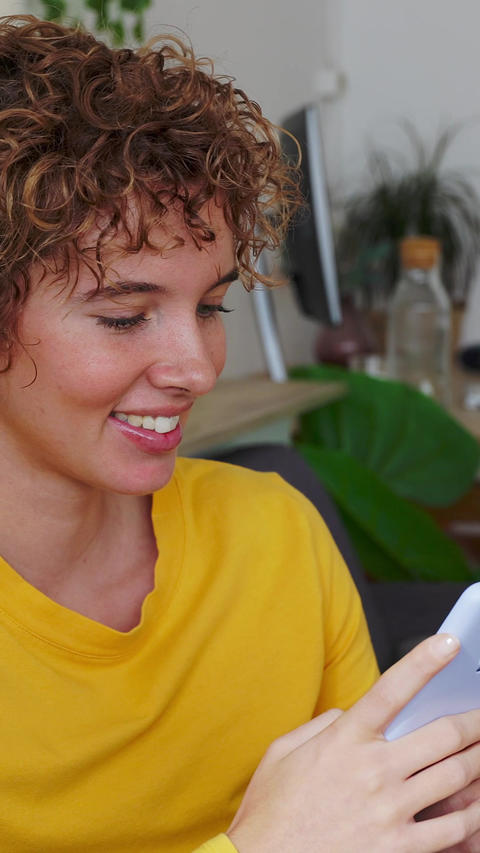 Young adult Latin American woman sitting relaxed on a sofa using smartphone