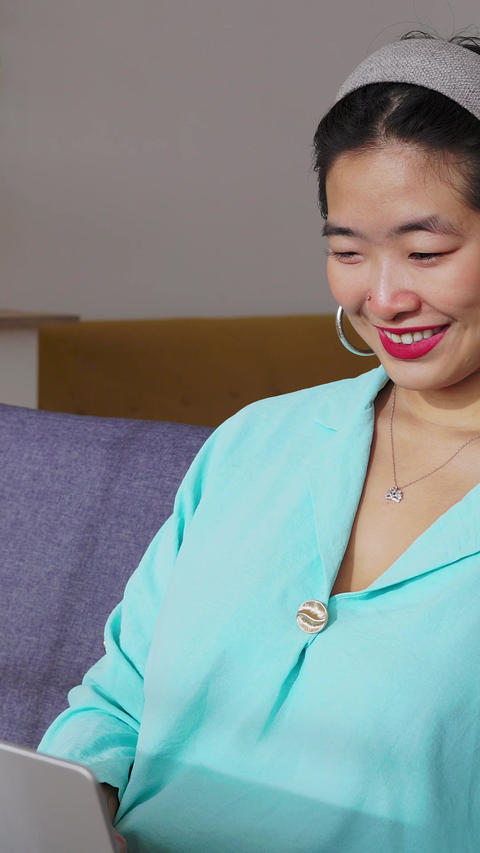 Young adult asian woman using laptop sitting comfortably on a sofa at home