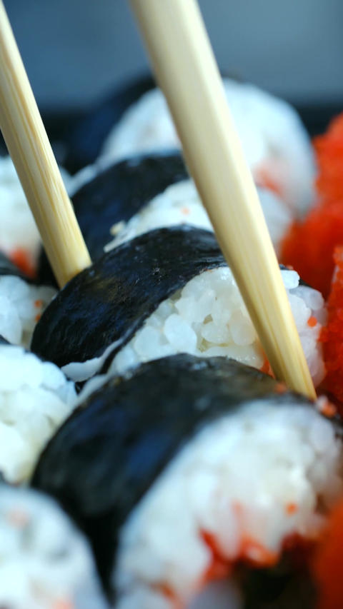 Person taking a fresh maki sushi roll with chopsticks