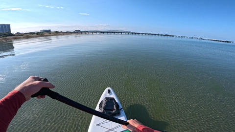 POV stand up paddleboarding on crystal clear sea water near coastline on a sunny