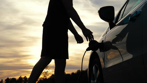 Man in golden hour disconnects EV charging at sunset