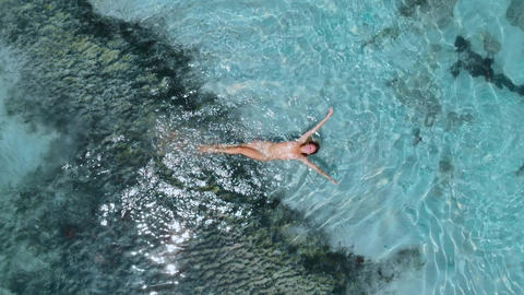 Young naked woman swims and floating in turquoise ocean. Aerial view, top view