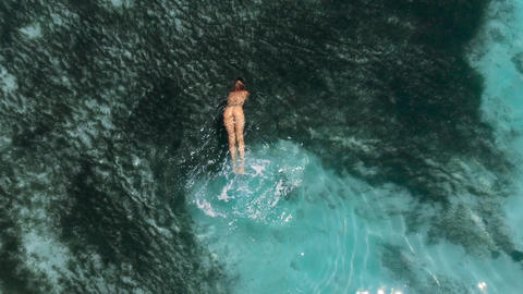 Young naked woman swims and floating in turquoise ocean. Aerial view, top view