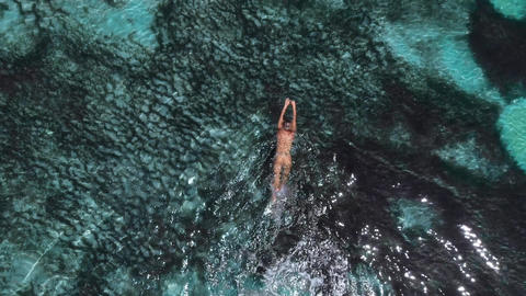 Young naked woman swims and floating in turquoise ocean. Aerial view, top view