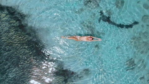 Young naked woman swims and floating in turquoise ocean. Aerial view, top view