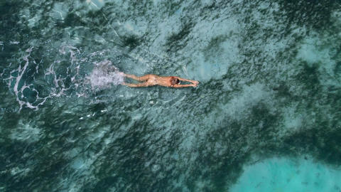 Young naked woman swims and floating in turquoise ocean. Aerial view, top view