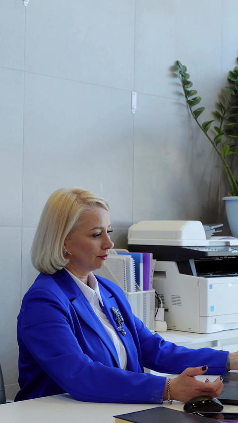 Businesswoman in a blue suit is working on a computer at her desk. She is using