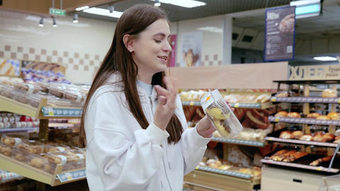 Young woman beams while selecting pastries in a supermarket bakery. Joy radiates