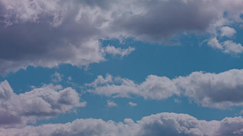 Bright cumulus clouds drifting across a calm blue sky in soft daylight