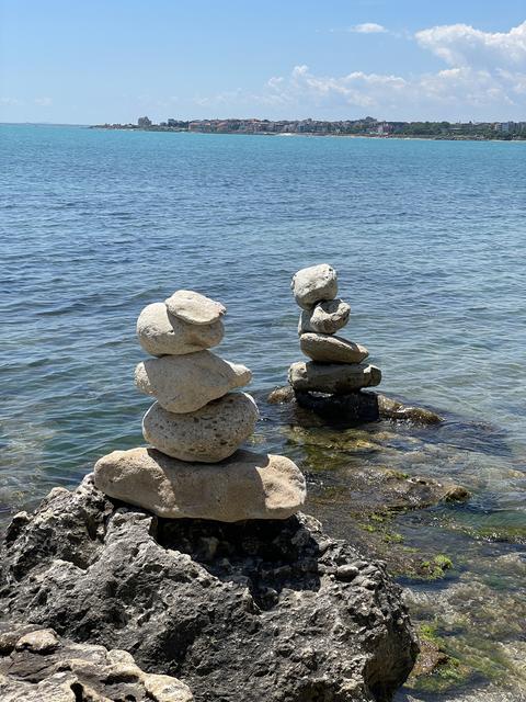 Balanced stone stacks on rocky seashore photo with turquoise sea, distant coastal town and blue sky