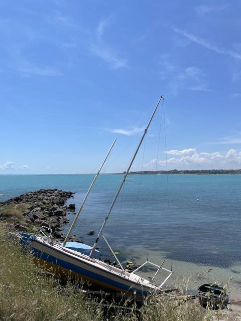 Sailboat on rocky seashore photo with blue sea, clear sky and coastal horizon, peaceful summer