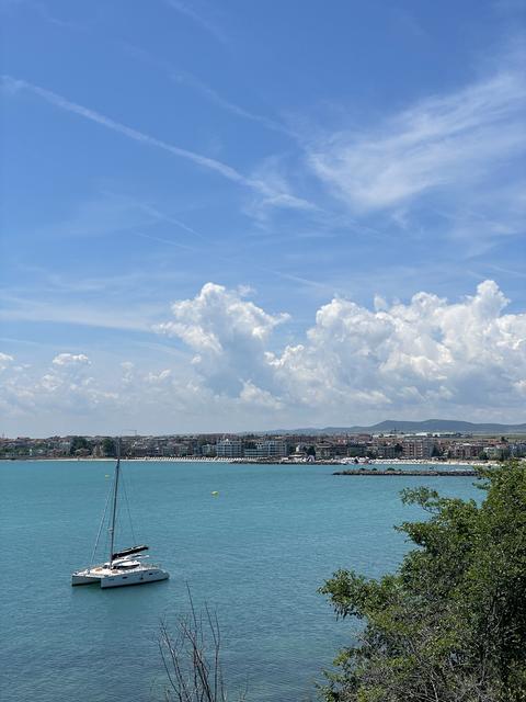 Sailboat on turquoise sea photo with coastal town, dramatic white clouds and blue sky, peaceful