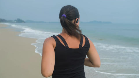 Athletic woman jogging by sea from behind